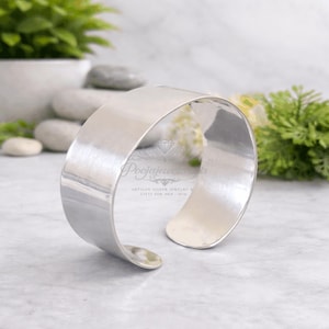 Pode incluir: Uma pulseira de punho larga e polida em prata. O design aberto apresenta uma superfície lisa e reflexiva. A pulseira é uma joia simples e elegante, adequada para o uso diário. A pulseira tem aproximadamente 5 cm de largura.