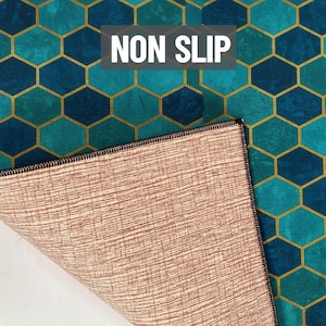 Puede incluir: Alfombra antideslizante con un patr&oacute;n geom&eacute;trico de panal de abeja en color turquesa y azul, con contornos dorados. La parte inferior de la alfombra es de color marr&oacute;n claro con un dise&ntilde;o texturizado. El texto "NON SLIP" se muestra en blanco.