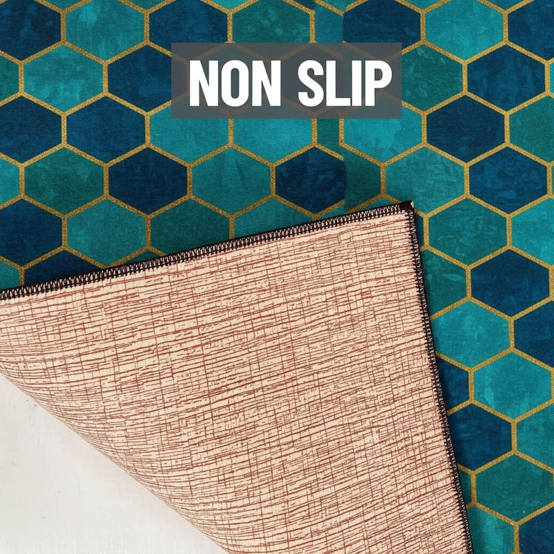 Puede incluir: Alfombra antideslizante con un patr&oacute;n geom&eacute;trico de panal de abeja en color turquesa y azul, con contornos dorados. La parte inferior de la alfombra es de color marr&oacute;n claro con un dise&ntilde;o texturizado. El texto "NON SLIP" se muestra en blanco.