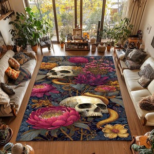 Op de afbeelding: Een groot vloerkleed met een donkerblauwe bloemen- en schedelontwerp. Het vloerkleed heeft grote roze en gele bloemen, gouden slangen en twee witte schedels. Het vloerkleed ligt in een woonkamer met twee witte banken en grote ramen.