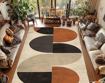 Puede incluir: Una alfombra grande con un diseño geométrico en un salón. La alfombra presenta óvalos superpuestos en negro, marrón y crema sobre un fondo claro de vetas de madera. La habitación tiene grandes ventanales y está amueblada con plantas y sofás. La alfombra mide unos 240 cm x 300 cm.