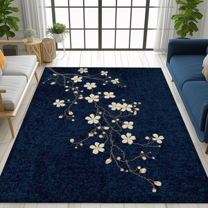 May include: A navy blue area rug featuring a floral branch design with white blossoms and buds. The rug is rectangular and placed on a light wood floor, with a sofa and window in the background.