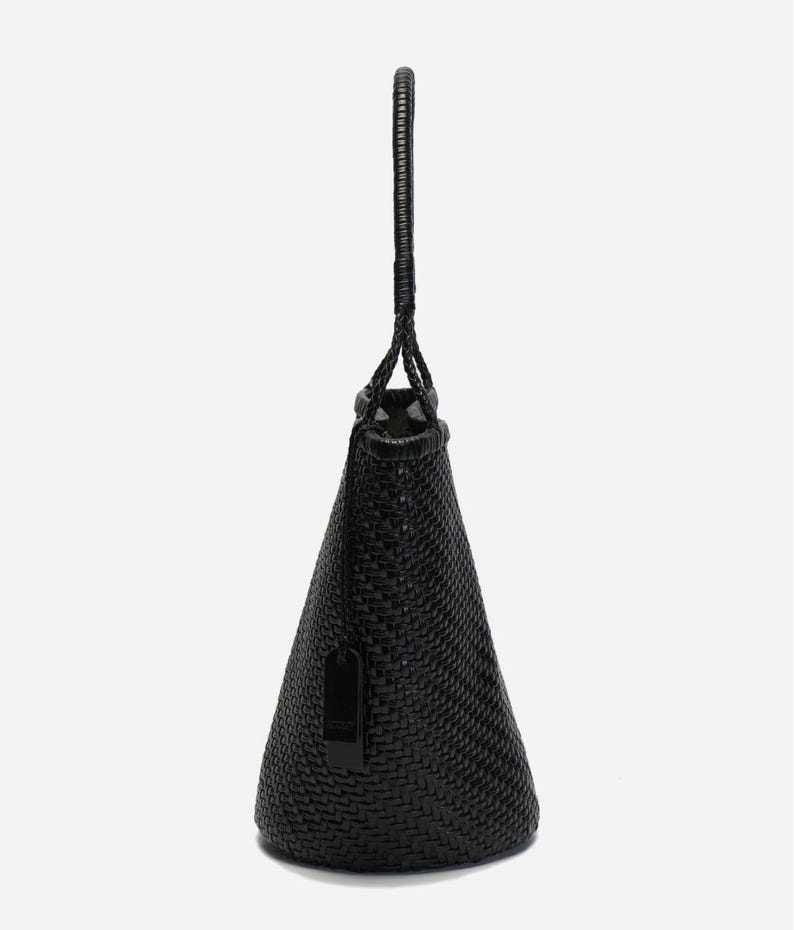 May include: Black woven tote bag with a braided handle. The bag has a conical shape and a small tag attached. The weave pattern is visible, and the bag appears to be made of a durable material.