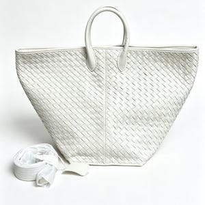 May include: A white woven leather tote bag with two top handles and a detachable shoulder strap. The bag has a trapezoid shape and a textured surface. The bag is made of white leather.