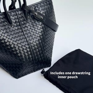 May include: Black leather tote bag with a woven design, featuring a top handle and a shoulder strap. Includes a black drawstring inner pouch. The bag is set against a white background.