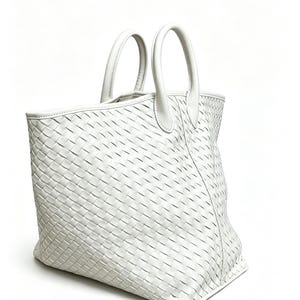 May include: A white tote bag with a woven design. The bag has two rounded handles and a rectangular shape. The material appears to be leather or a leather-like material. The bag is set against a white background.