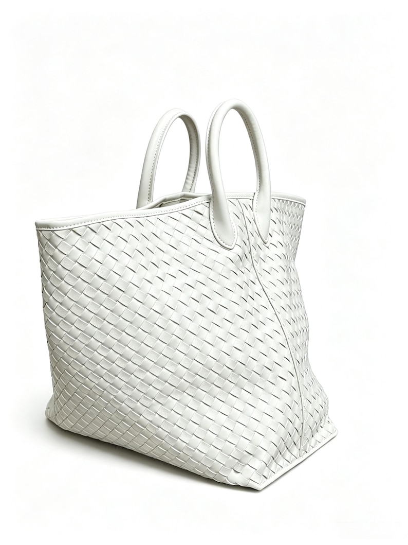 May include: A white tote bag with a woven design. The bag has two rounded handles and a rectangular shape. The material appears to be leather or a leather-like material. The bag is set against a white background.