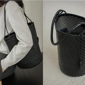 May include: A black woven tote bag with a cylindrical shape and a single handle. The bag is made of a tightly woven material, and the handle is a darker shade of black. The bag is shown being carried over the shoulder.