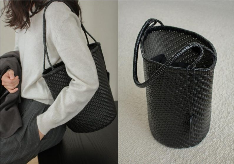 May include: A black woven tote bag with a cylindrical shape and a single handle. The bag is made of a tightly woven material, and the handle is a darker shade of black. The bag is shown being carried over the shoulder.