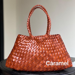 May include: A caramel-colored woven tote bag with braided handles. The bag is made of a tightly woven material, creating a textured appearance. The word "Caramel" is printed on the bag.