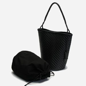 May include: A black woven bucket bag with a matching drawstring pouch. The bag has a single handle and a small tag. The weave pattern is visible on the bag's exterior. The pouch is made of a soft, opaque material.