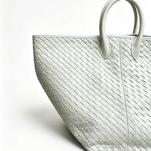 May include: A light gray tote bag with a woven pattern. The bag has two rounded handles and a rectangular shape. The bag is made of a soft material and is suitable for carrying various items.