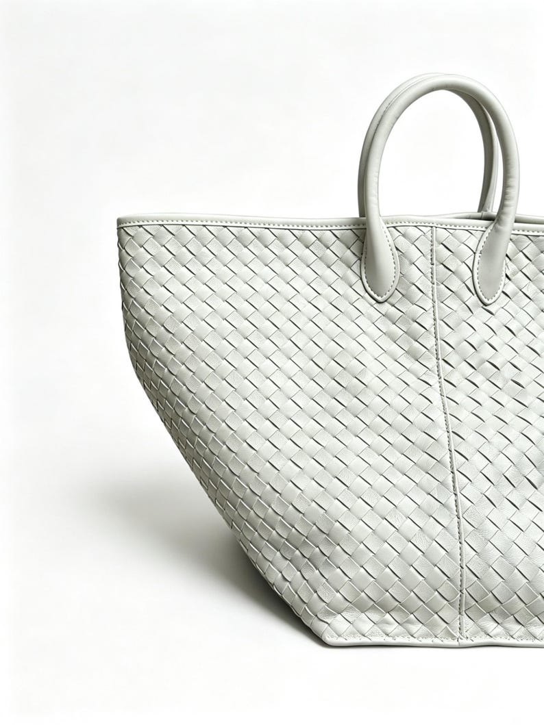 May include: A light gray tote bag with a woven pattern. The bag has two rounded handles and a rectangular shape. The bag is made of a soft material and is suitable for carrying various items.