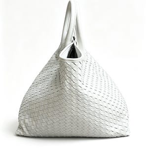 May include: A white woven leather tote bag with a single handle. The bag has a large, open top and a woven pattern throughout the body. The handle is curved and attached to the top of the bag. The bag is made of a soft, pliable leather.