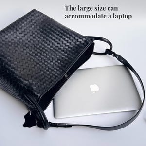 May include: Black woven leather tote bag with a long shoulder strap. The bag is open, revealing a silver laptop inside. The text on the image reads: "The large size can accommodate a laptop."