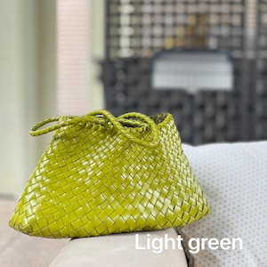 May include: Light green woven handbag with braided handles. The bag features a basket weave design and a trapezoid shape. The text "Light green" is visible at the bottom of the image. The bag is sitting on a light-colored surface.