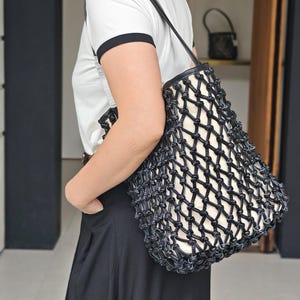 Puede incluir: Bolso tote negro y blanco con un diseño único en forma de red. El bolso tiene un exterior tejido negro y un interior blanco. La correa es negra y el bolso se lleva al hombro. Un accesorio elegante.