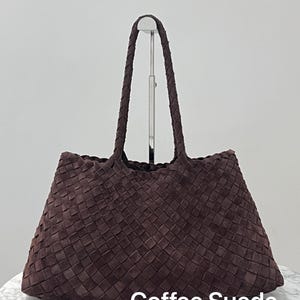 May include: A brown suede tote bag with a woven design. The bag has two braided handles and the text "Coffee Suede" at the bottom. The bag is displayed on a white surface.