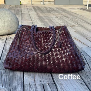 May include: A large, woven leather tote bag in a deep coffee brown color. The bag features a braided handle and a spacious interior. The word "Coffee" is printed in white at the bottom of the bag.