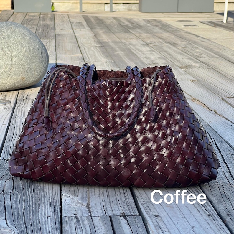 May include: A large, woven leather tote bag in a deep coffee brown color. The bag features a braided handle and a spacious interior. The word "Coffee" is printed in white at the bottom of the bag.