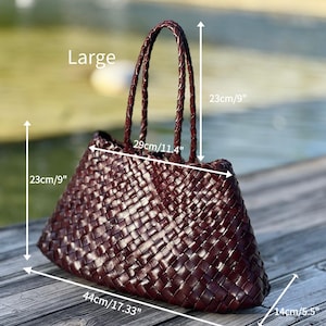 May include: A large, woven burgundy tote bag with braided handles. The bag measures 17.33 inches wide, 9 inches high, and 5.5 inches deep. The handles are 11.4 inches long. The bag is displayed outdoors.