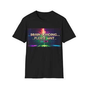 May include: Black t-shirt featuring the text "BRAIN LOADING.. PLEASE WAIT.." in a pixelated font. The graphic includes a digital loading bar in shades of purple, green, and orange, creating a vibrant, tech-inspired design.