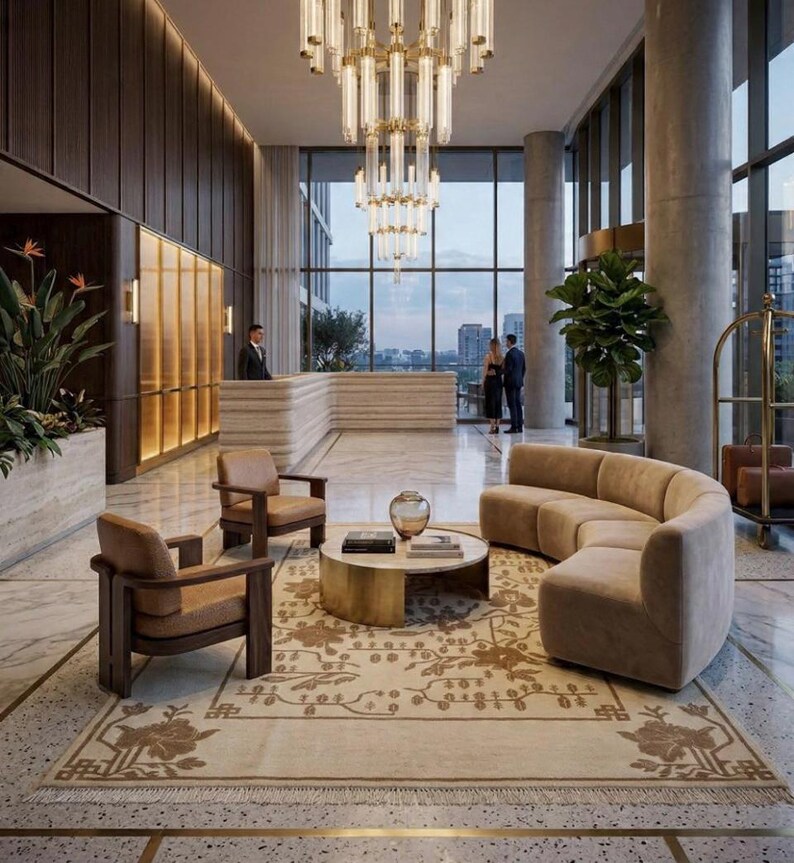 May include: A luxury hotel lobby with a grand chandelier, reception desk, and seating. The room includes a curved sofa, two armchairs, and a round coffee table on a patterned rug. Large windows provide a city view.