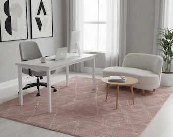 May include: A modern home office setup featuring a white desk, gray office chair, and a small round table. A light pink rug with a geometric pattern covers the floor. A curved sofa and artwork complete the room's decor.