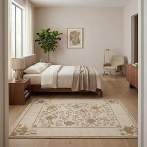 May include: A bedroom with a bed featuring cream bedding and a brown wooden frame. A beige rug with a floral design is on the wooden floor. A side table with a lamp and a potted plant complete the room's decor, creating a calm atmosphere.
