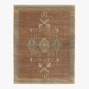 Puede incluir: Una alfombra rectangular de color óxido con un diseño geométrico central en dorado y gris. El diseño presenta formas de diamante, triángulo y flecha. La alfombra tiene un borde estampado y bordes con flecos, adecuada para la decoración del hogar.