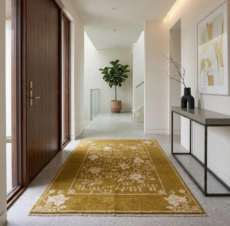 Pu&ograve; includere: Tappeto rettangolare giallo senape con un motivo floreale in un corridoio. Il tappeto ha un bordo e un motivo floreale color crema. Il corridoio presenta una porta in legno, una consolle e una pianta in vaso. Il tappeto misura circa 183 cm per 274 cm.