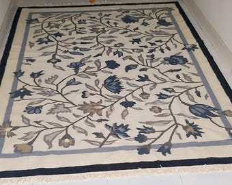 May include: Cream-coloured rectangular rug featuring a floral pattern in shades of blue, grey, and brown. The rug has a dark blue border and a light blue inner border. The floral design features stylised flowers and leaves.
