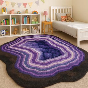 Könnte beinhalten: Ein großer, geodenförmiger Teppich mit einem dunkelbraunen Außenrand und konzentrischen Schichten aus Lila, Lavendel und Weiß. Die Mitte ist tiefblau mit weißen Sprenkeln, die an eine Sternennacht erinnern. Dieser Teppich ist ein dekorativer Bodenbelag.