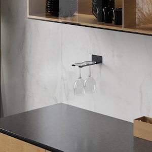 Può includere: Un portabicchieri in metallo nero montato su una parete bianca. Due bicchieri da vino trasparenti sono appesi al portabicchieri. Il portabicchieri è progettato per contenere due bicchieri. Lo sfondo presenta un piano di lavoro e un armadietto con tazze nere.
