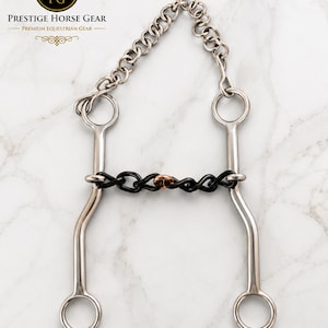 May include: A silver-coloured metal horse bit featuring two long shanks with rings at the top and bottom, connected by a black chain mouthpiece with a central copper-coloured link. A silver curb chain is attached to the top rings of the bit.