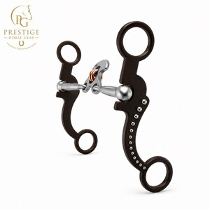 Pode incluir: Um freio para cavalo com hastes curvas castanho-escuras e uma série de pequenos tachas prateadas ao longo da borda externa. O bocal é de metal prateado com um elo central de rolo na cor cobre, ligado a dois anéis.