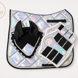 Pode incluir: Um tapete de sela acolchoado com acabamento prateado holográfico e rebordo preto, acompanhado por uma touca de croché preta com detalhes holográficos e um par de protetores de perna holográficos a condizer com tiras pretas e forro polar branco.