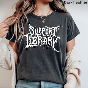以下が含まれることがあります： 白の「SUPPORT YOUR LOCAL LIBRARY」の文字がスタイリッシュなフォントでプリントされた、ダークヘザーグレーのTシャツ。クルーネックと半袖のデザイン。全体的にカジュアルで着心地の良いスタイル。