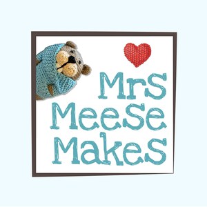 May include: A brown crocheted bear wearing a light blue crocheted sweater with a red crocheted heart in the background. The text "Mrs Meese Makes" is written in blue.