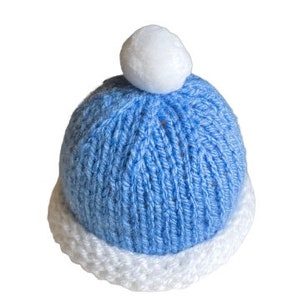 May include: A blue knitted baby hat with a white pom pom on top. The hat has a white brim.