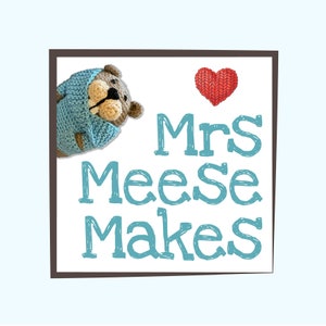 May include: A brown crocheted bear wearing a light blue crocheted sweater with a red crocheted heart in the background. The text "Mrs Meese Makes" is written in blue.