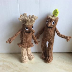 May include: Two knitted brown tree figures with smiling faces. One figure has a brown knitted crown and the other has a green leaf on top of its head.