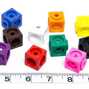 May include: A selection of brightly coloured plastic cubes in shades of blue, brown, white, purple, red, orange, green, yellow, black, and pink. Each cube features different geometric shapes and circular connectors.