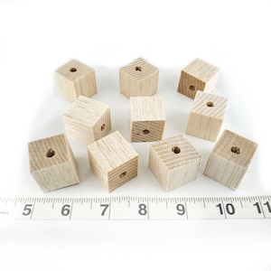 May include: Ten wooden cubes with a hole drilled through the center of each. The cubes are arranged in a random pattern on a white surface.