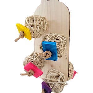 May include: Wooden bird toy with five hanging woven balls. The balls are attached to the wood with string and have colorful square pieces of wood attached to the string.