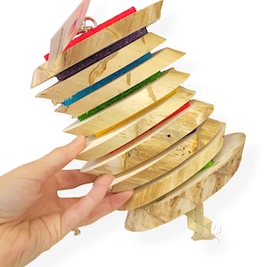 May include: A colorful wooden bird toy with a rainbow of colors, including red, orange, yellow, green, blue, and purple. The toy is made of natural wood and has a rope hanging from the bottom.