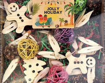 May include: A foraging toy set for birds, featuring a wooden gingerbread man, a wooden Christmas tree, and a variety of natural materials, including pine cones, wood chips, and colorful balls. The set is packaged in a cardboard box with a label that reads "Foraging Flats Jolly Holiday".