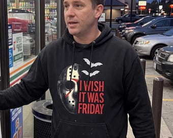May include: A black hooded sweatshirt featuring a graphic of a hockey mask, two white bats, and the red text "I WISH IT WAS FRIDAY" printed on the chest. The hoodie has long sleeves, a front kangaroo pocket, and a drawstring hood.