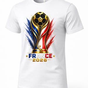 May include: White t-shirt featuring a gold and black soccer ball trophy design with blue, white, and red accents. The text "FRANCE 2026" is displayed below the trophy. A sporty design.