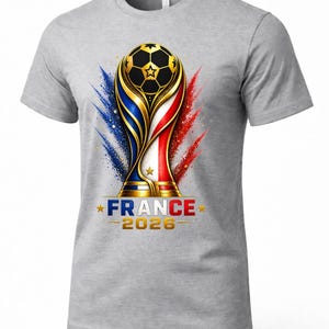 May include: Gray t-shirt featuring a soccer trophy design with a soccer ball, and the text "FRANCE 2026". The trophy design incorporates the colors of the French flag, with blue, white, and red accents.